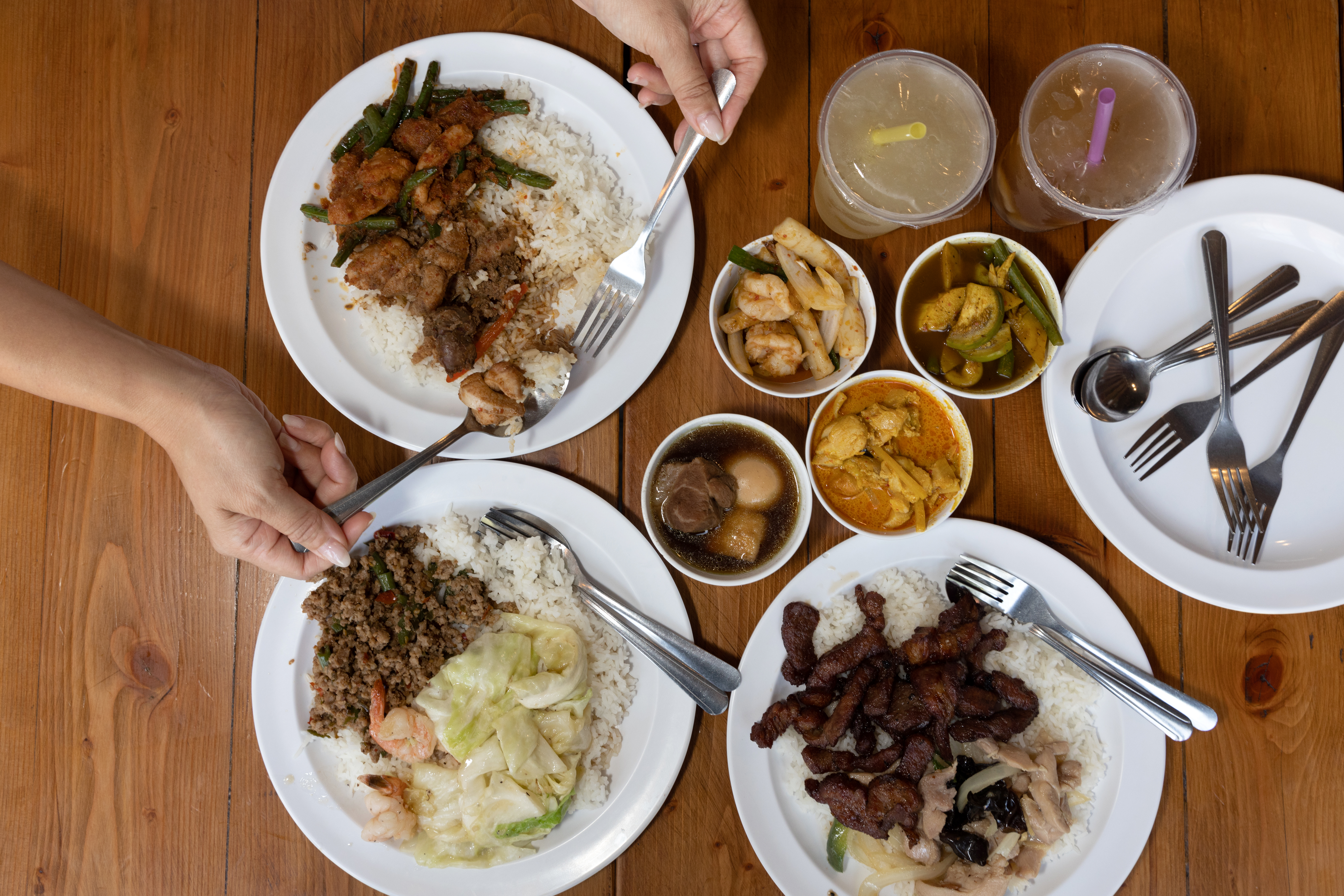 Four dishes of Thai food on white plates on a wooden table.