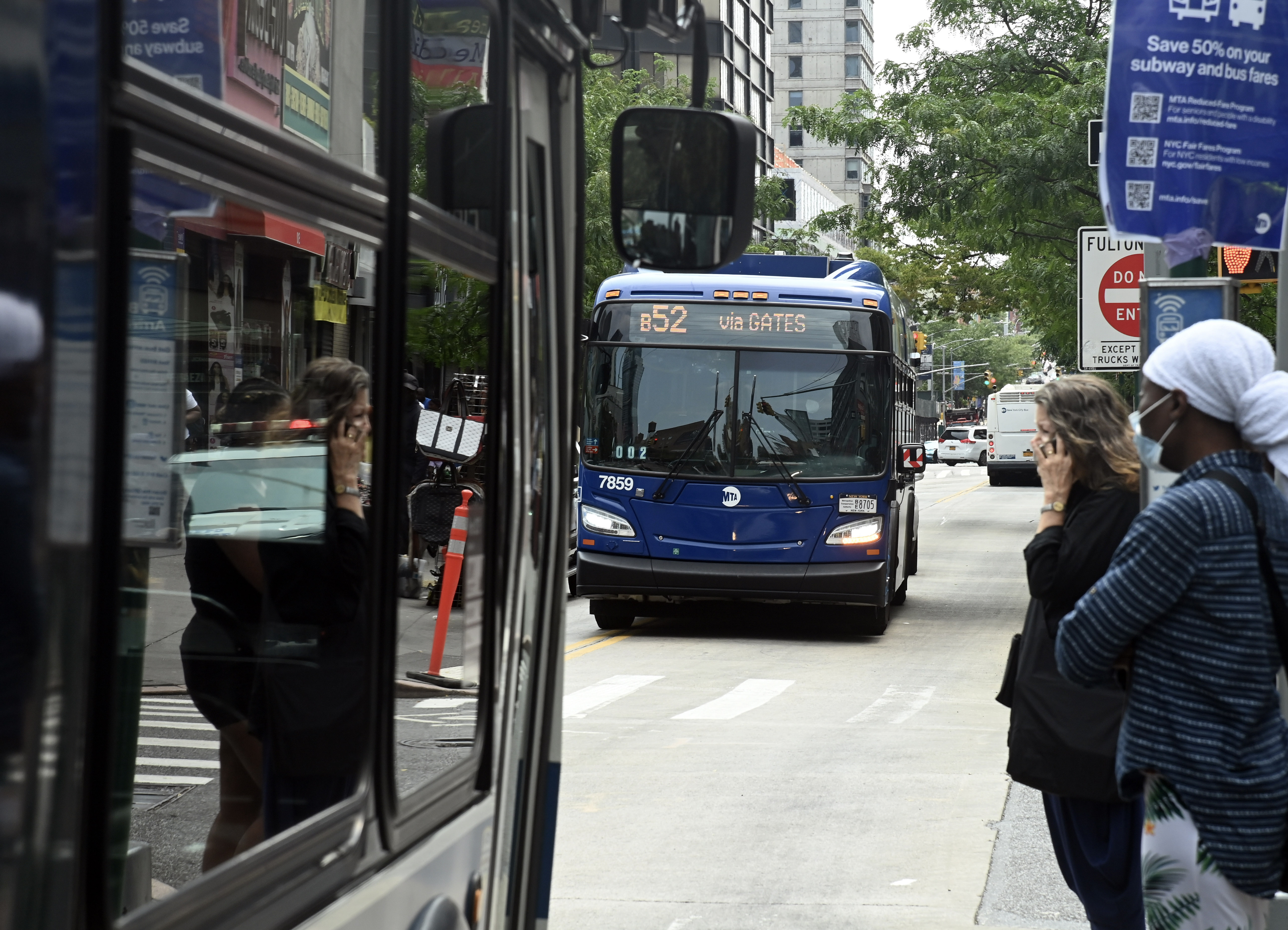 A photo of two riders waiting for a bus to arrive in Brooklyn.