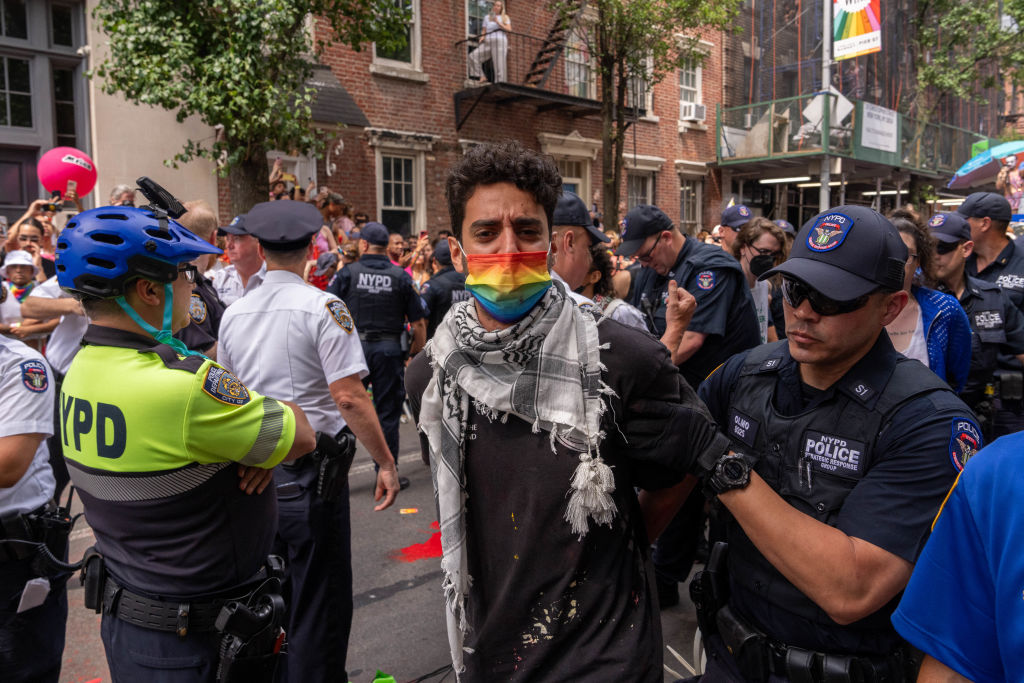 A demonstrator wearing a rainbow face mask is detained by police.