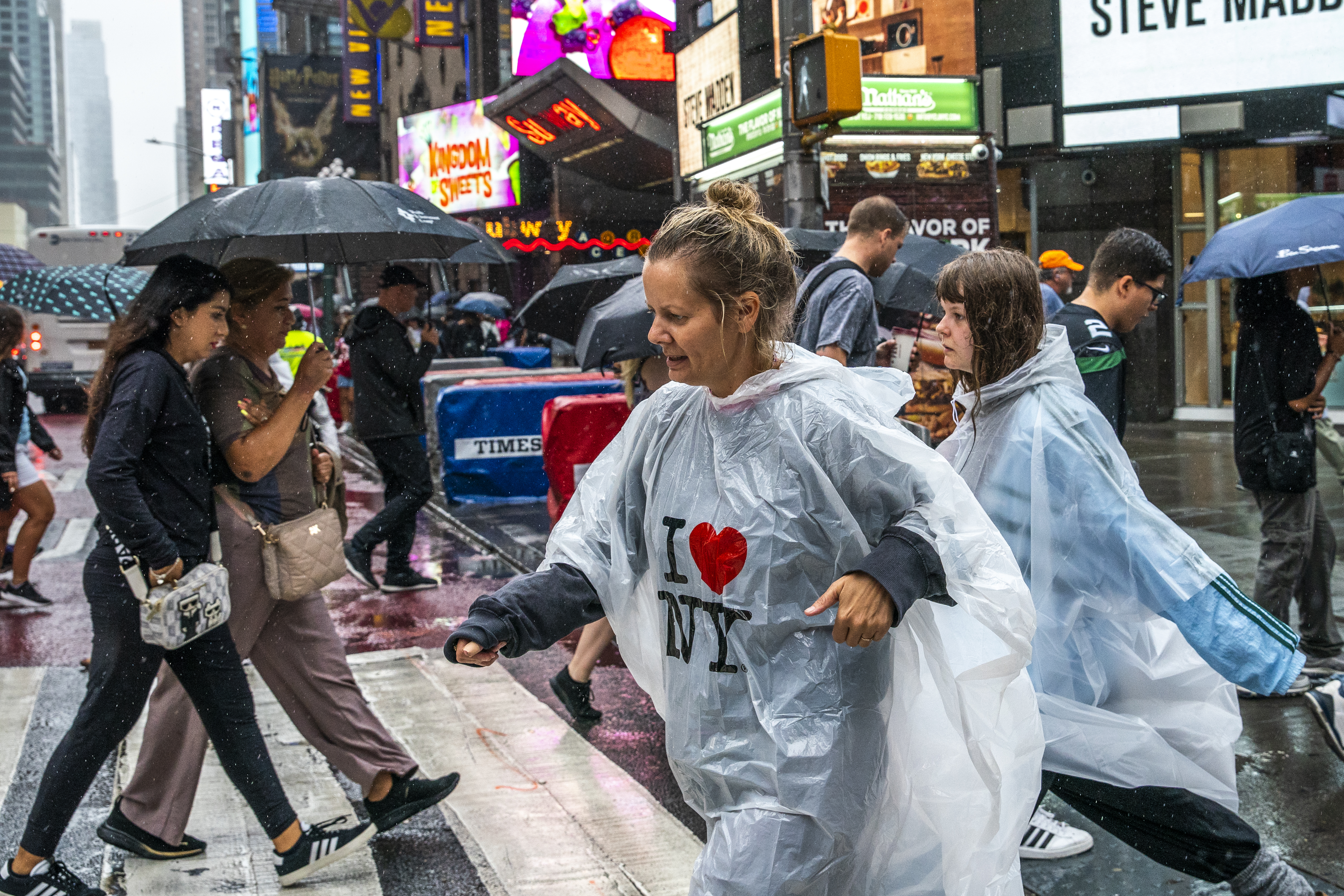 People walk around Times Square with umbrellas and rain slicks