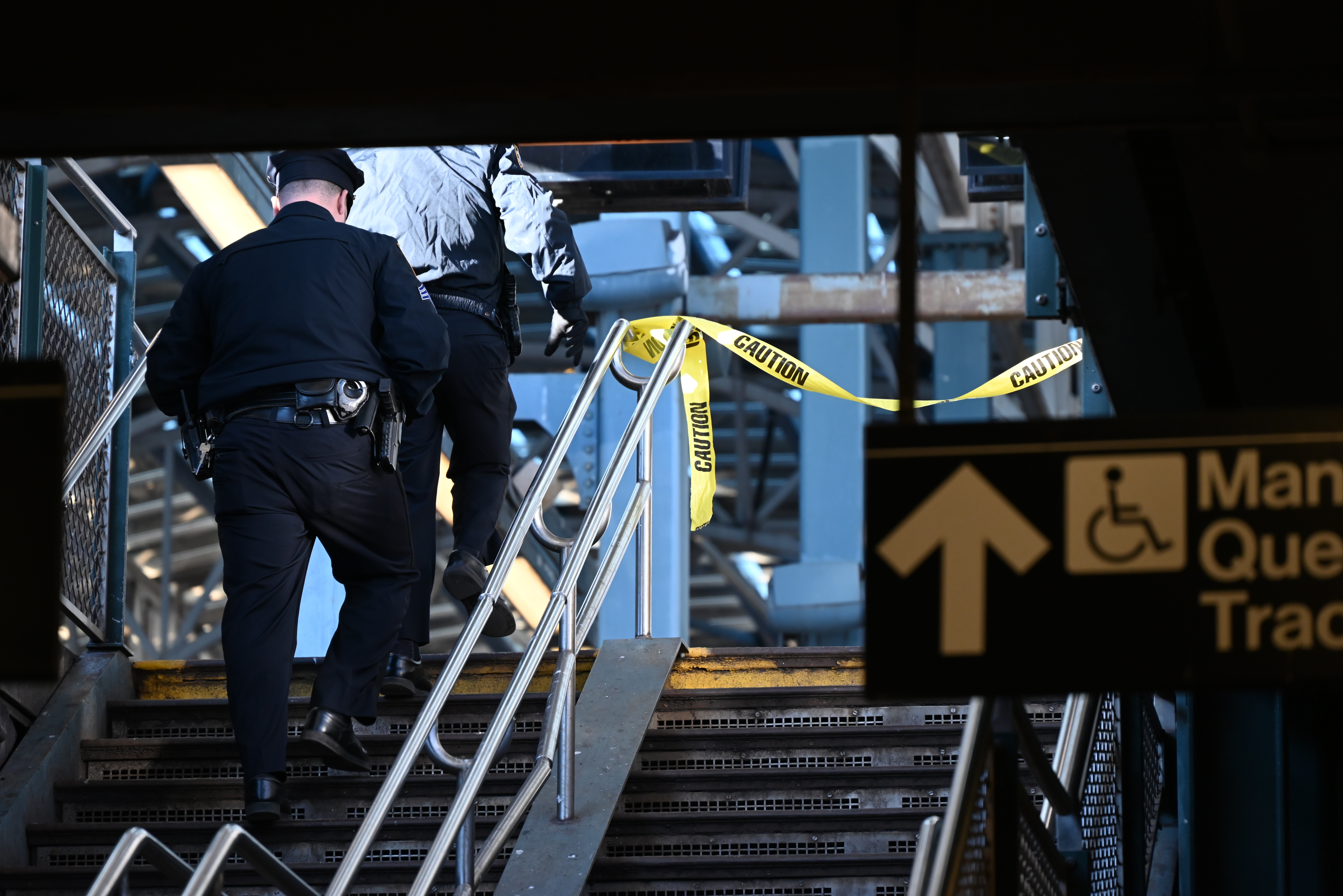 Police officers climb subway stairs alongside police tape.