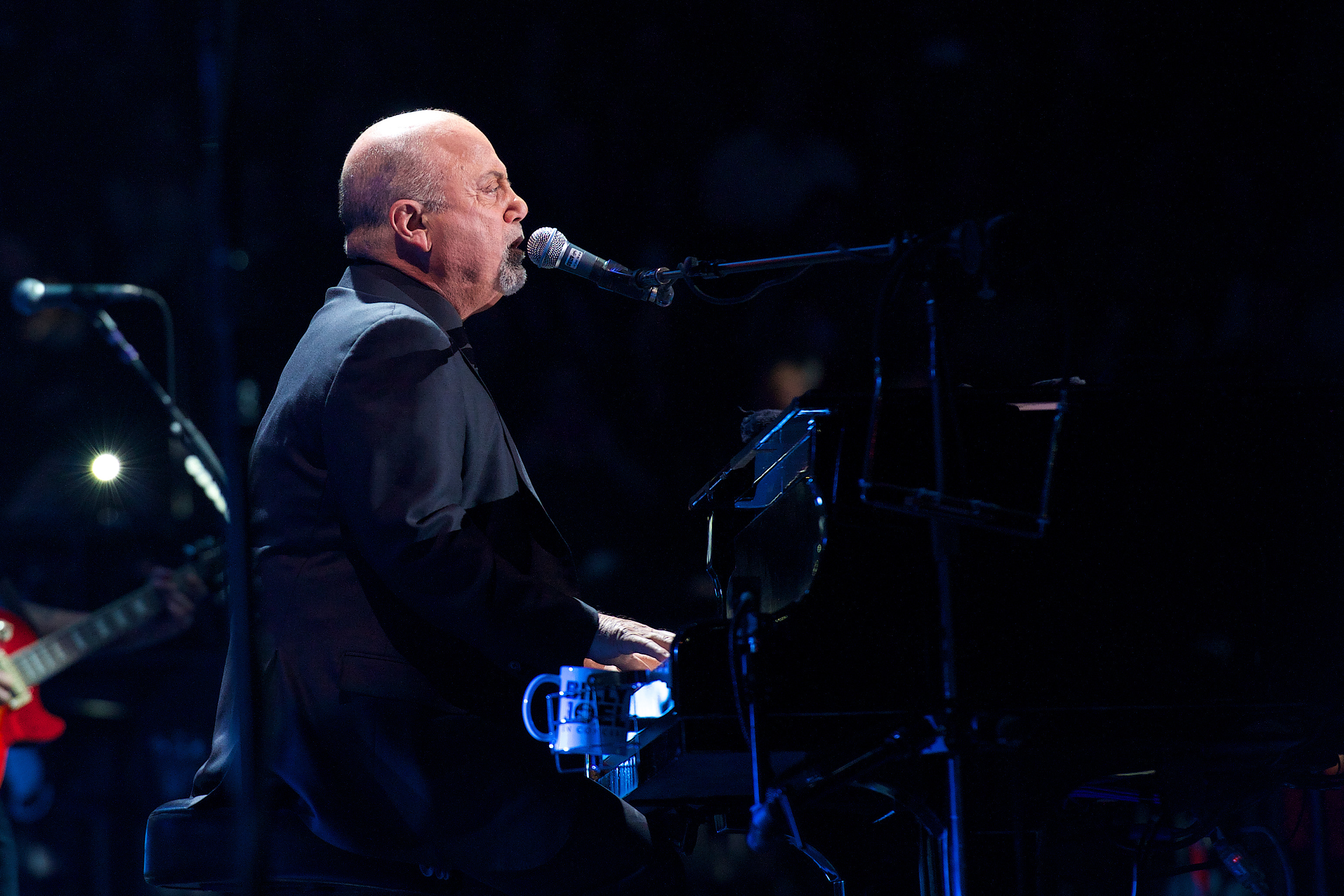 A man plays the piano while singing into a microphone.