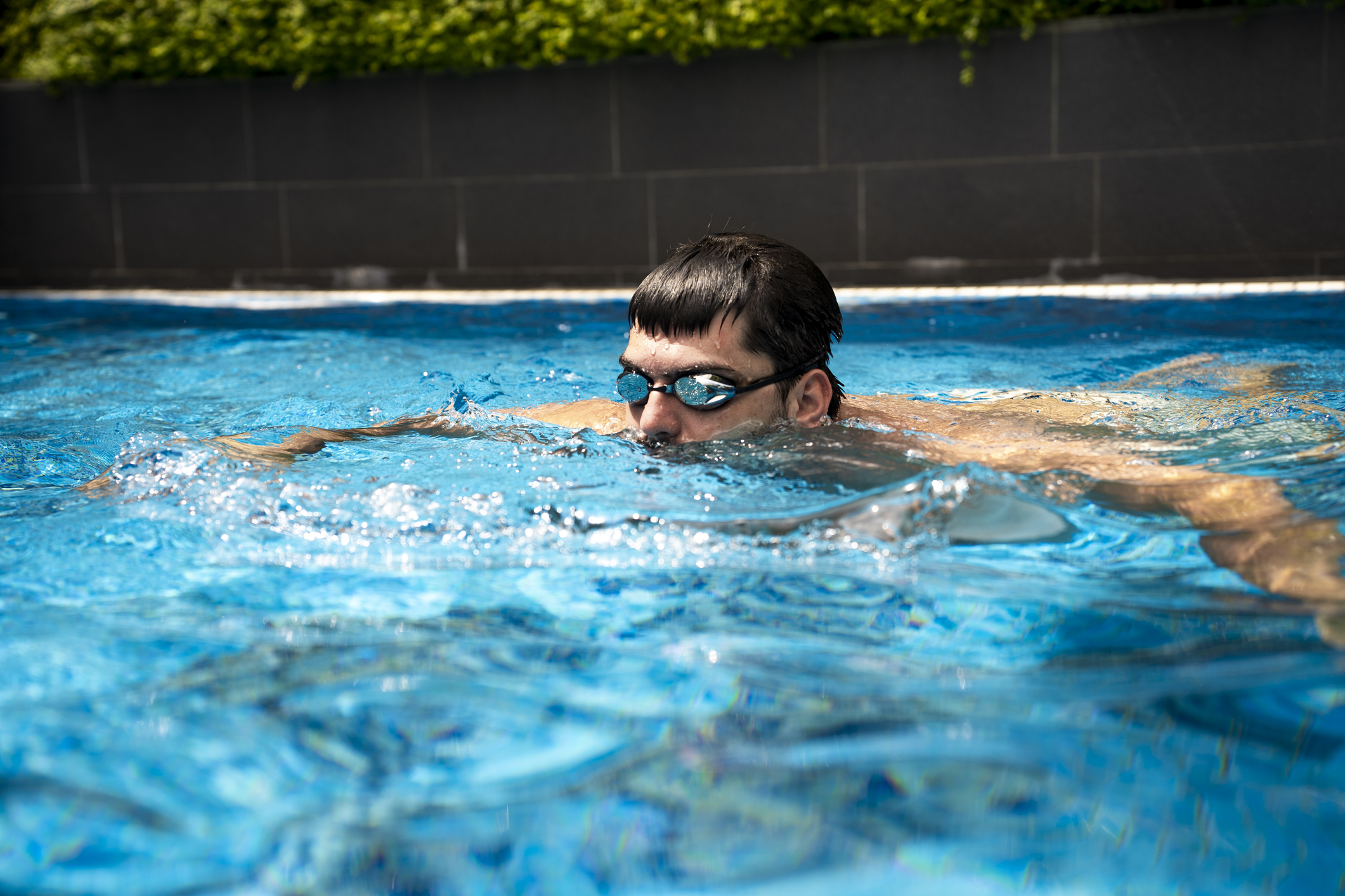a guy with goggles on pokes his head above the pool water