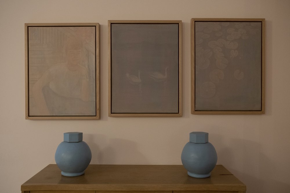 Two urns sit beneath two paintings.