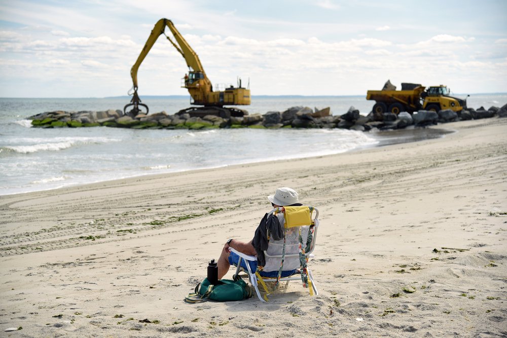 A beachgoer on the Rockaway Peninsula in Queens sits next to a construction site, where a new jetty is being built. Photo taken June 28, 2022