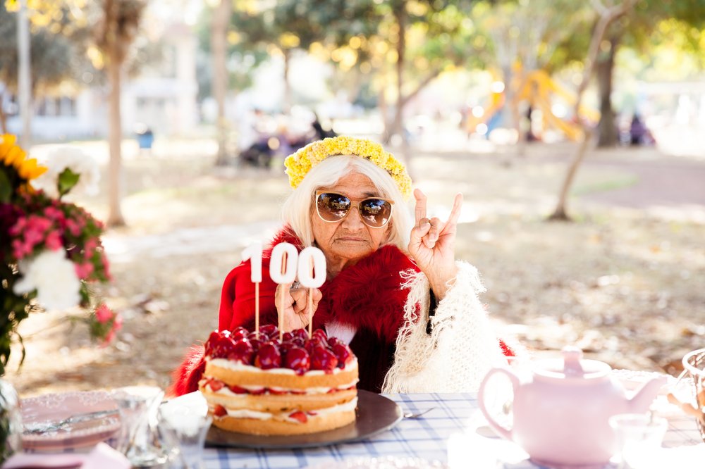an elderly woman with a birthday cake and candles that say "100"