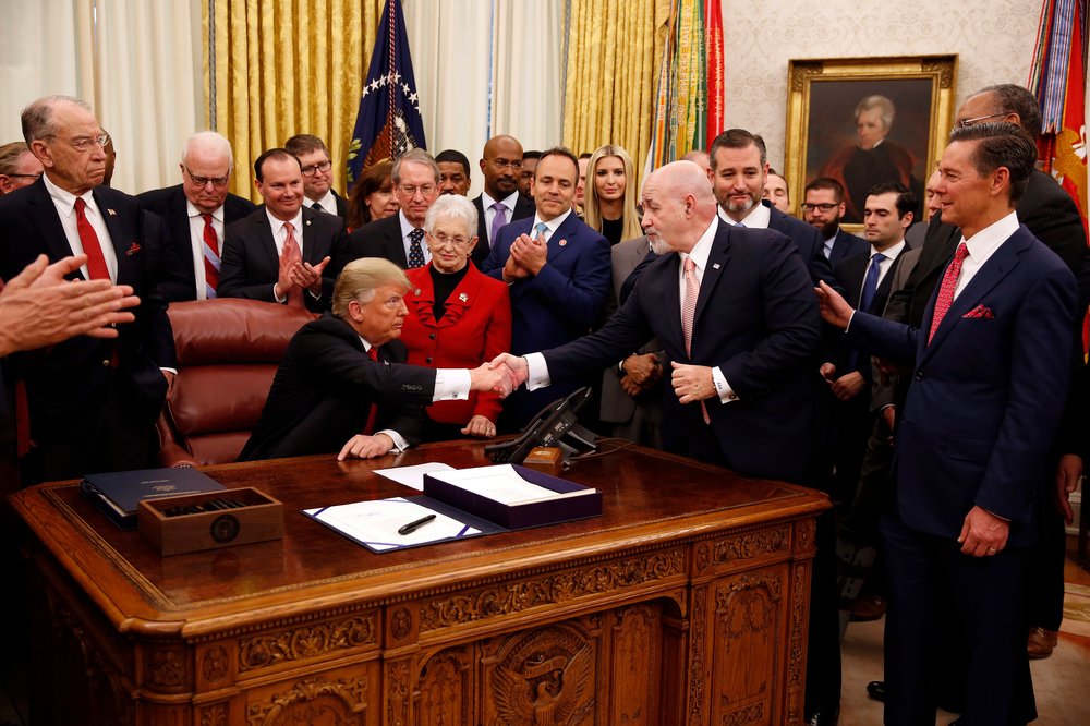 A photo of former NYPD commissioner Bernard Kerik and President Donald Trump shaking hands in the Oval Office during a bill signing December 21, 2018 surrounded by a group of people.