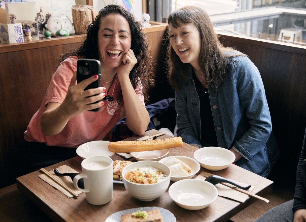 Two people smile at a booth in a restaurant surrounded by plates of food.