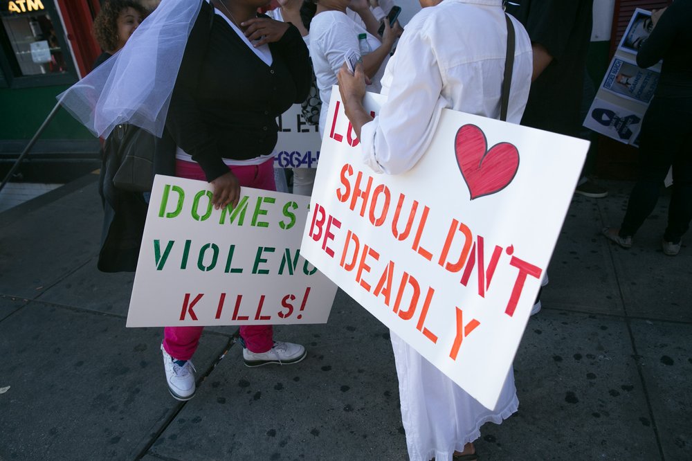 Demonstrators hold signs saying "domestic violence kills" and "love shouldn't be deadly."