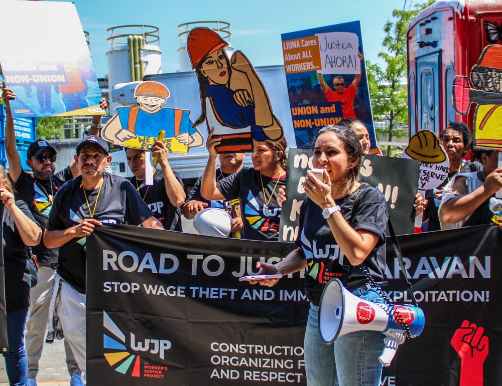 People protest, holding signs including "Justice Ahora" and "Stop wage theft and immigrant exploitation."