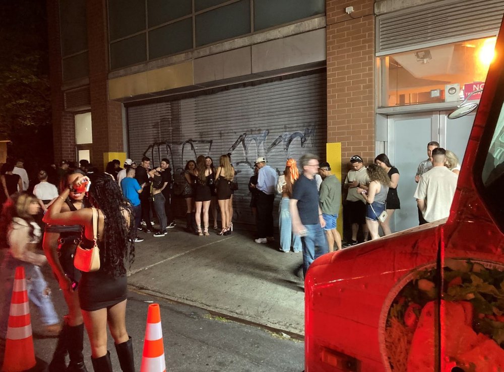 Crowds of people wait in line on a sidewalk.