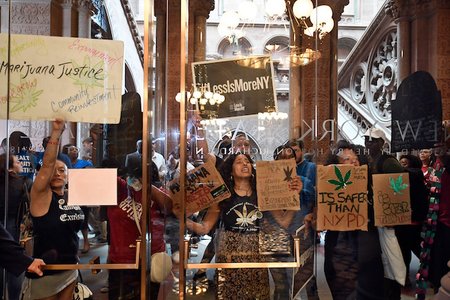 Protesters urging legislators to pass Marijuana legislation holds a signs against the senate lobby doors at the state Capitol, in Albany, N.Y.