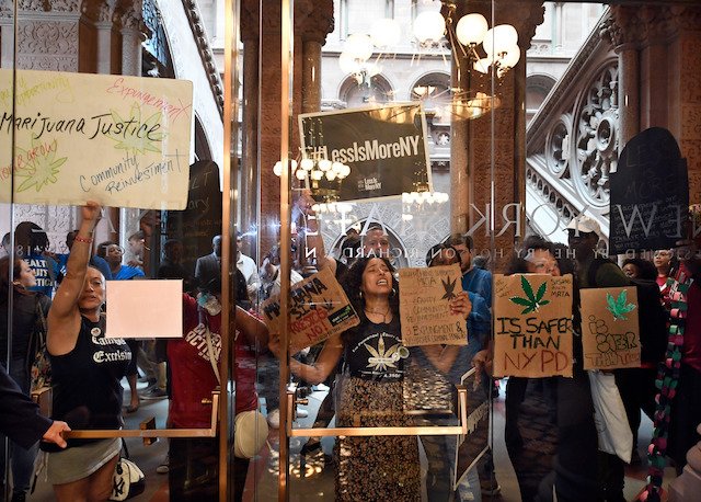 Protesters urging legislators to pass Marijuana legislation holds a signs against the senate lobby doors at the state Capitol, in Albany, N.Y.
