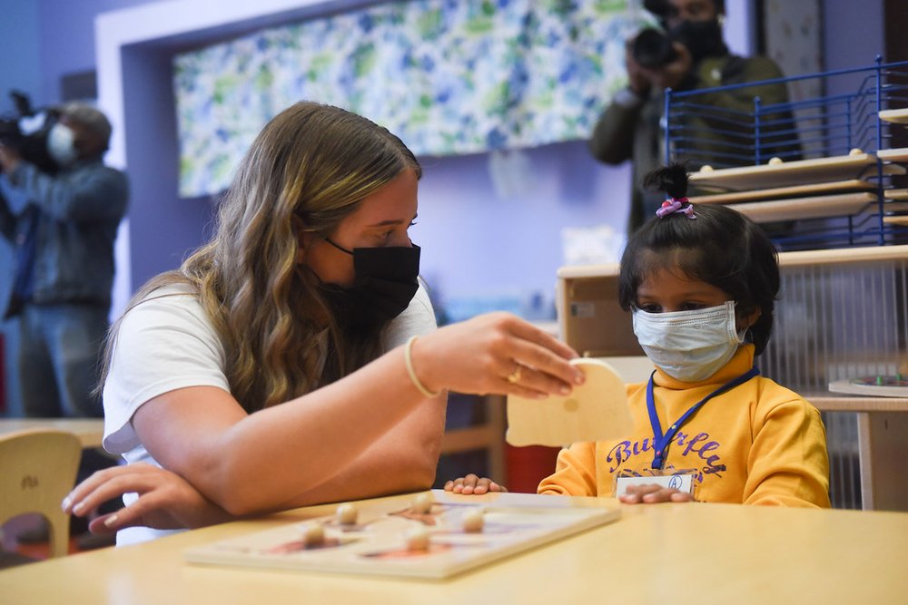 a teacher and student, both wearing masks, sit at a table