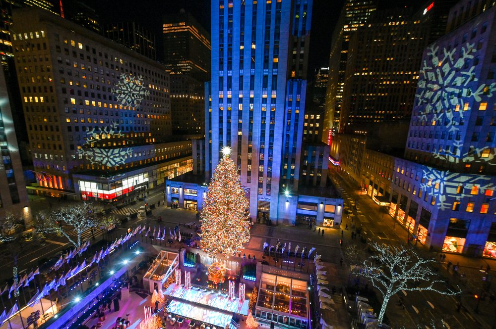 The Rockefeller Center tree is lit in multi-colored lights, within Rockefeller Center buildings