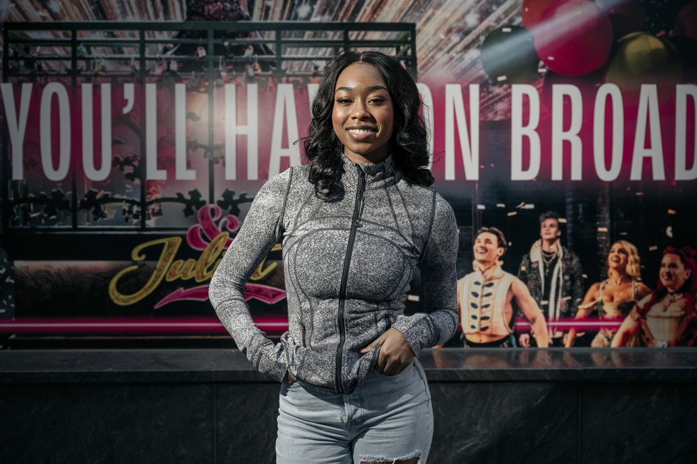 A woman smiles standing in front of a Broadway sign.