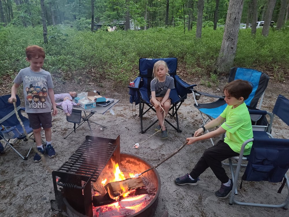 Six-year-old Seamus (center) and his two siblings sit around a fire on a recent camping trip. Their mom, Taylor Naughton, who enrolled Seamus in a Lyme disease vaccine trial, said she checks her kids for ticks frequently.