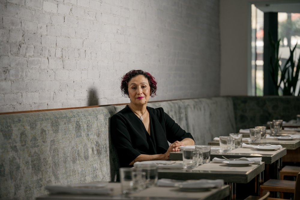 A woman sits in a large, sunlit dining room.