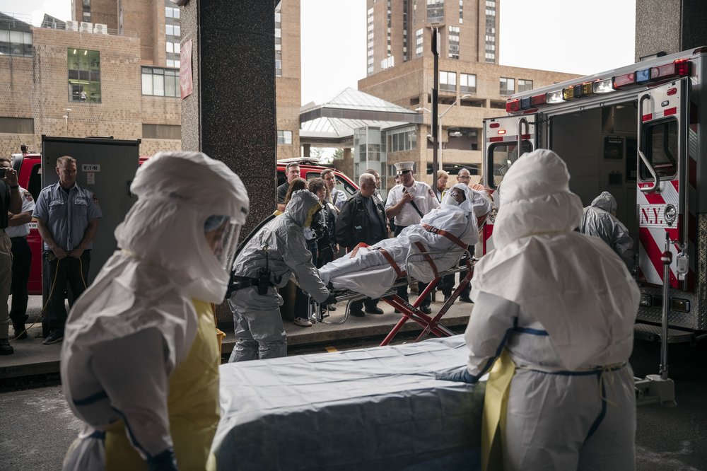 A patient covered in protective gear is rolled into an ambulance.