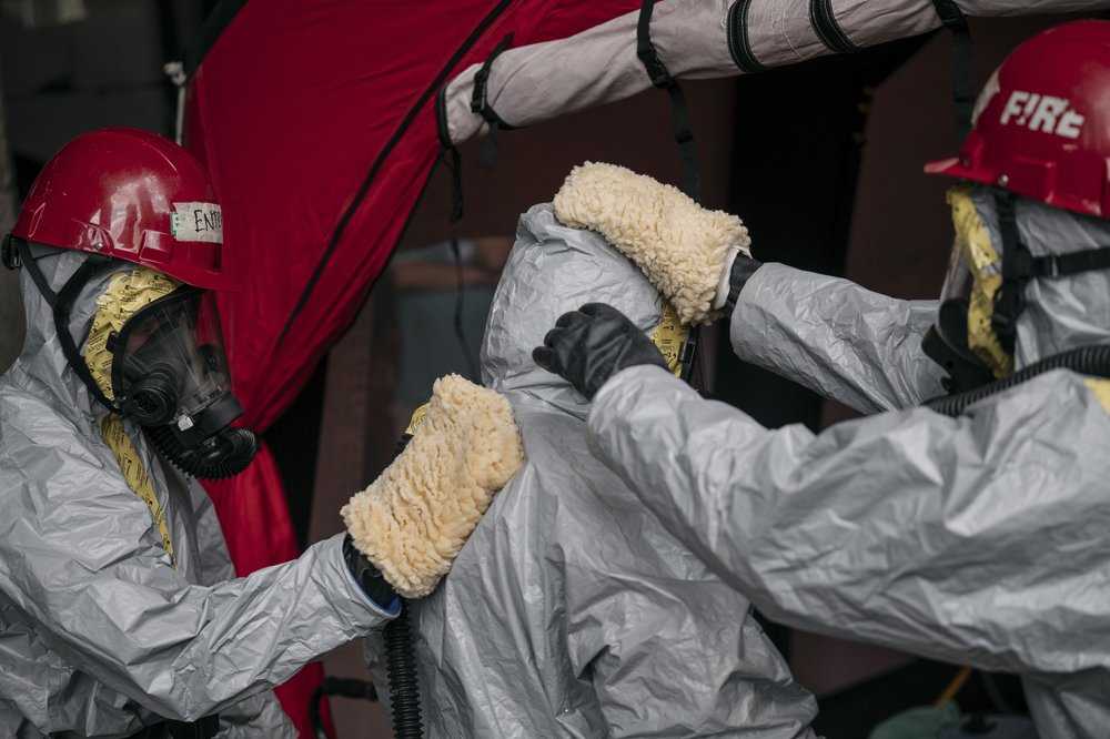 Two clinicians in hazmat suits use fuzzy-looking gloves to wipe down another clinician.