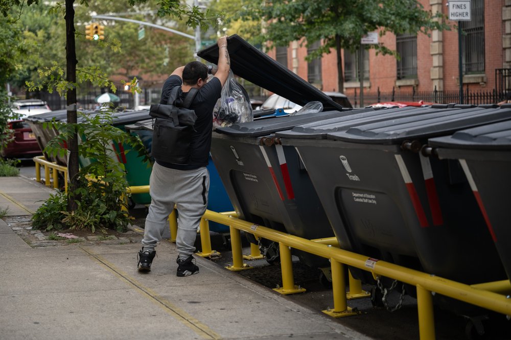 A person carried out a bag of trash from PS/IS 210 and tossed it into the new bins, Aug. 16, 2023.