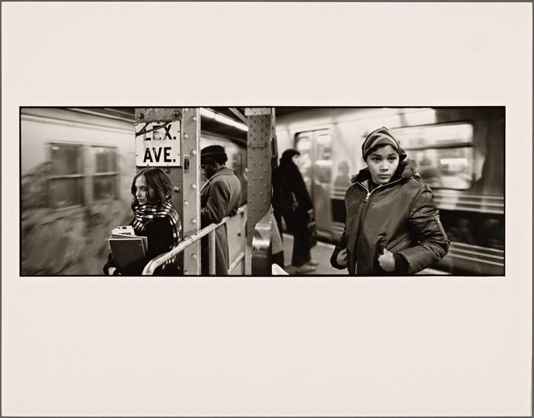 Two women look away from each on a subway platform, with trains in the background traveling toward each other.