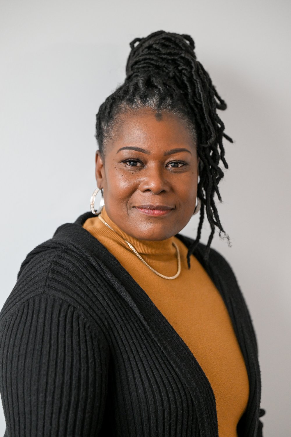 A headshot of a woman with an orange shirt and black sweater.