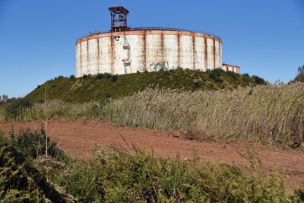 The neighboring liquid natural gas (LNG) facility, along Chemical Lane, is privately owned. The property is currently being remediated, to remove illegally dumped materials, which has interrupted plans to demolish the LNG tanks.