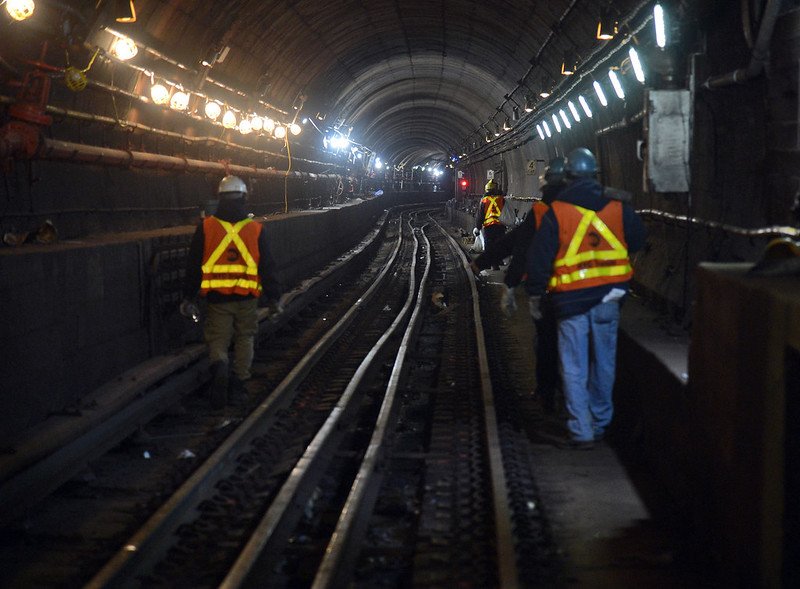 MTA workers wearing reflective vests walk along the subterranean E train subway tracks in NYC.