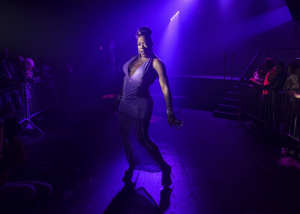 A person wearing a dress stands in spotlight, about to dance.
