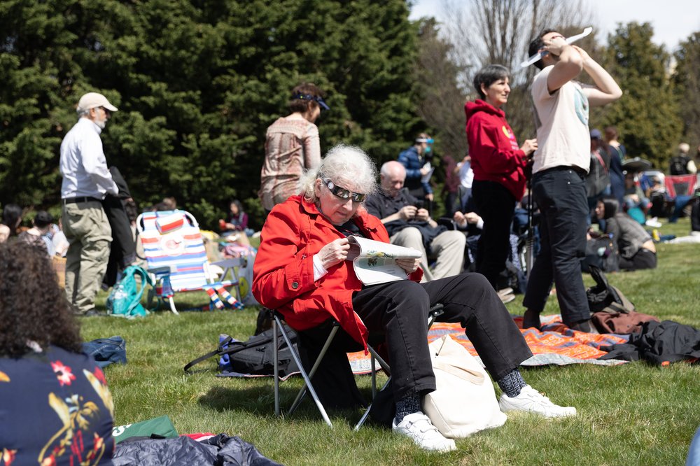 Susan Zugaib looks through eclipse glasses while reading before the solar eclipse at Greenwood Cemetery in Brooklyn.
