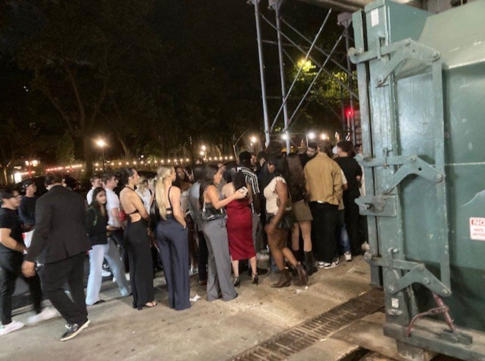 Crowds of people wait in line on a sidewalk.