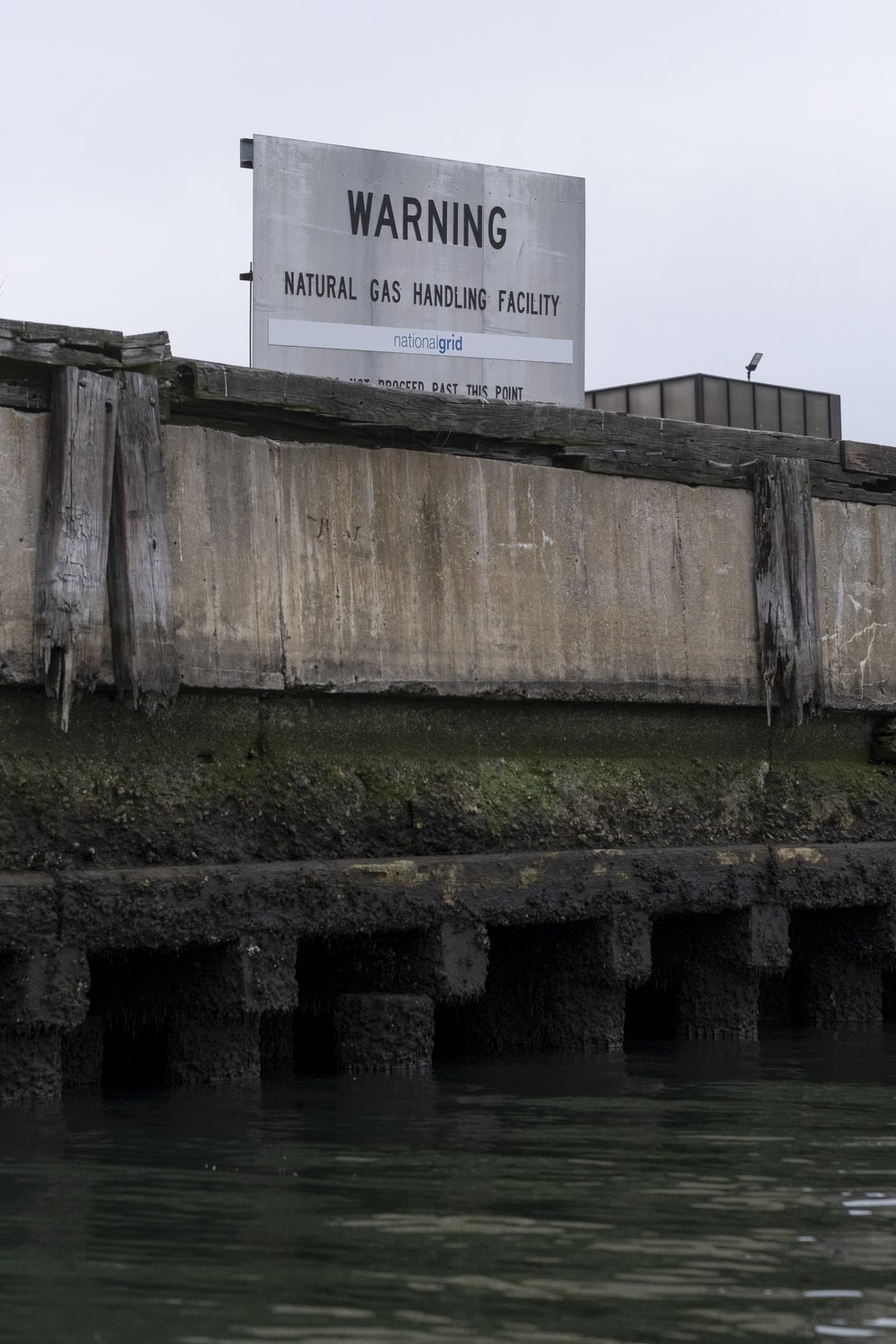 A sign above the creek reads: "Warning Natural Gas Handling Facility."