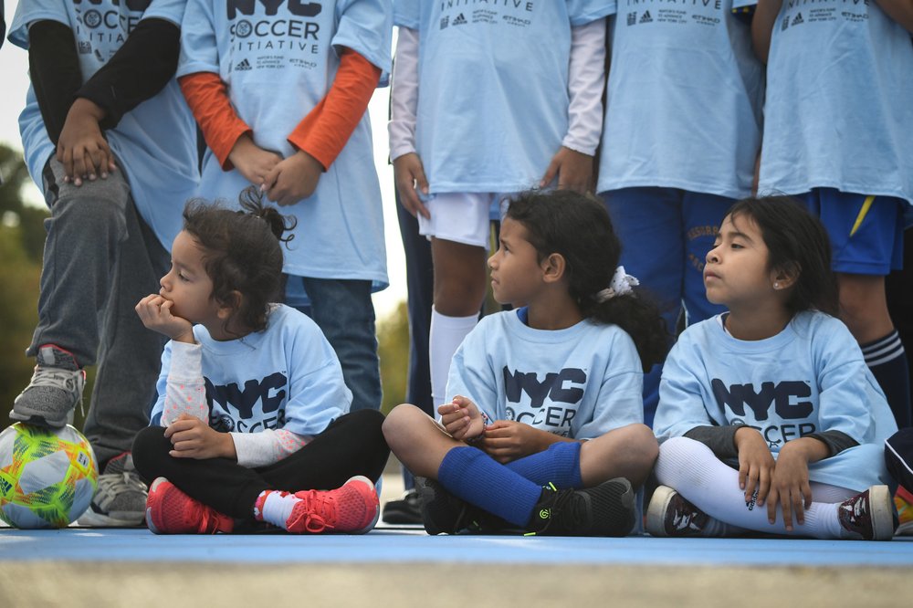 Children wait on the sidelines of a soccer game.