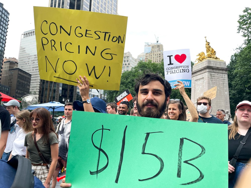 A demonstrator holds a sign reading "$15 billion."