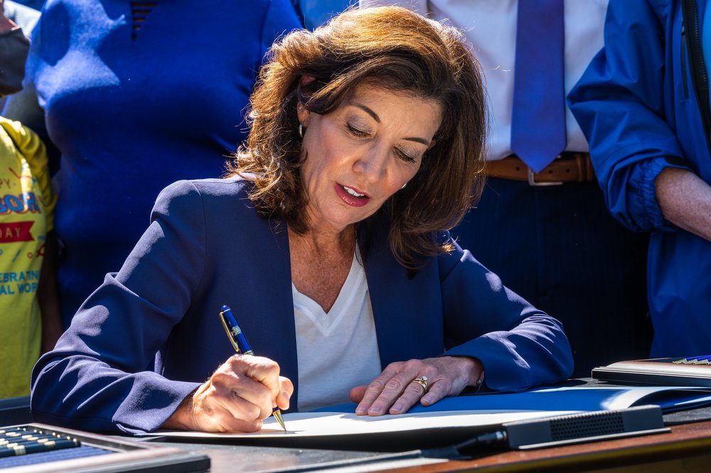 Governor Kathy Hochul, in a blue jacket, signs a bill