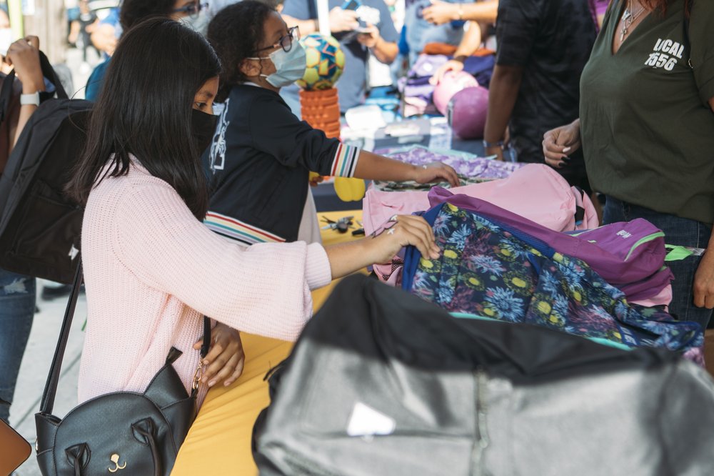 Kids check out backpacks piled on tables.