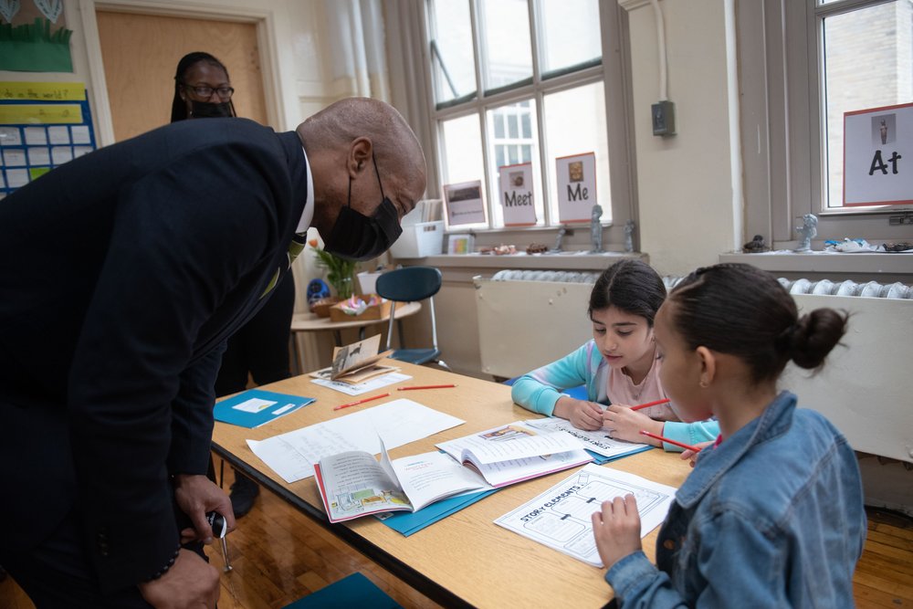 Mayor Eric Adams speaks to young kids at a table in a school.