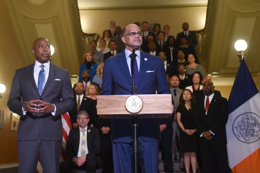 Schools Chancellor David Banks and Mayor Eric Adams speak at a press conference with a large crowd in the background.