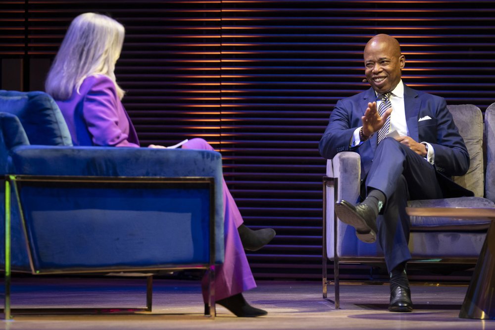 Mayor Eric Adams speaks with an interviewer while sitting in a chair onstage.