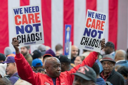 Henry Singleton with Local 1199 SEIU holds signs reading "We need care not chaos" at a rally coordinated by New York Governor Andrew Cuomo and House Minority Leader Nancy Pelosi in 2017