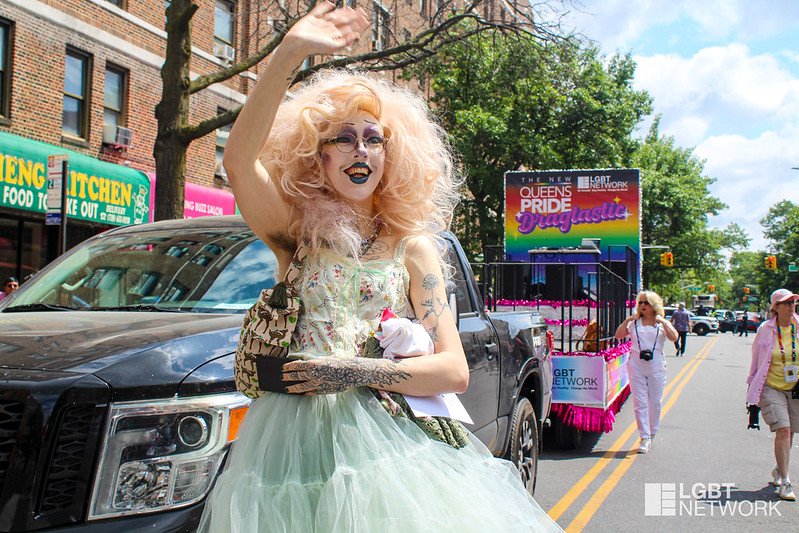A person in a green dress walks down the street, smiling.