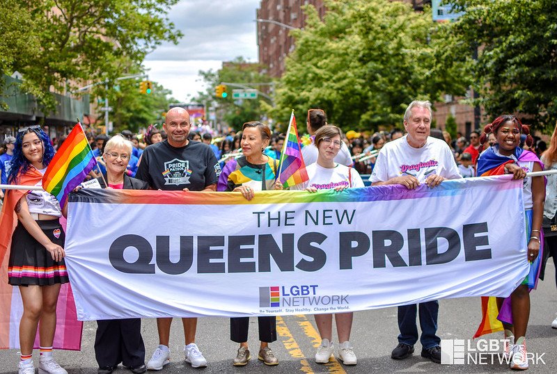 A group of people holding a sign that says "Queens Pride."