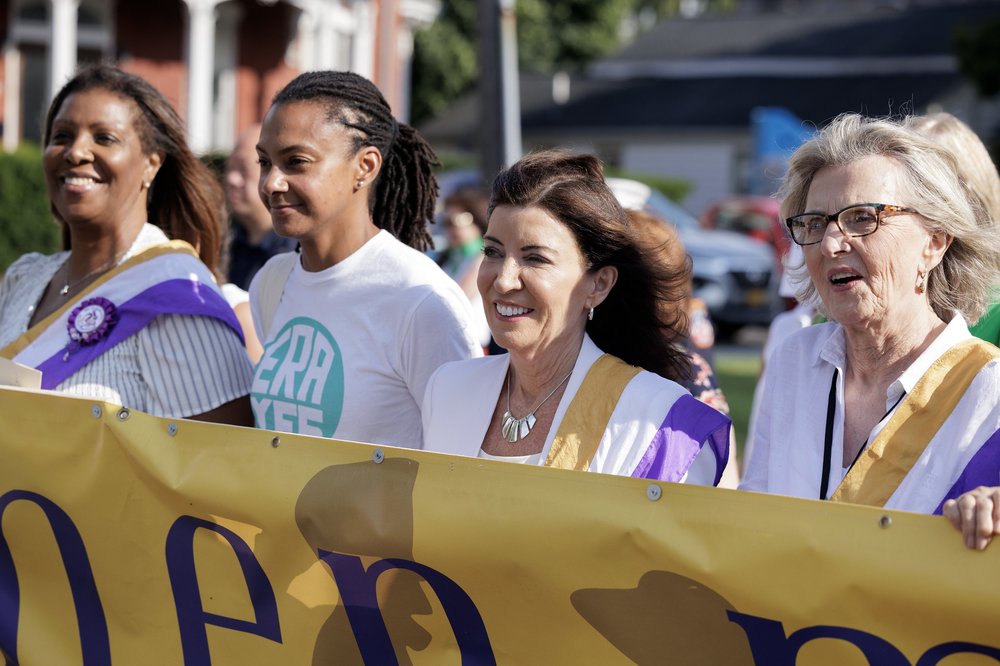 Gov. Kathy Hochul and Attorney General Letitia James, flanked by supporters, wear white and march at the 175th anniversary of the Seneca Falls Convention.