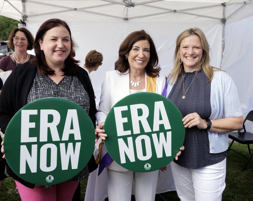 Governor Kathy Hochul stands with two women holding buttons that say ERA NOW