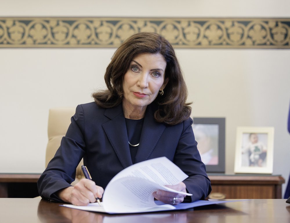 Governor Kathy Hochul stares into the camera while signing bills.