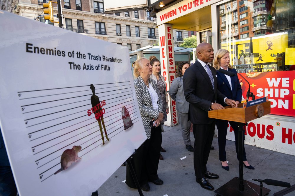Mayor Adams at a rat-related press conference, standing by a poster reading "the axis of filth."