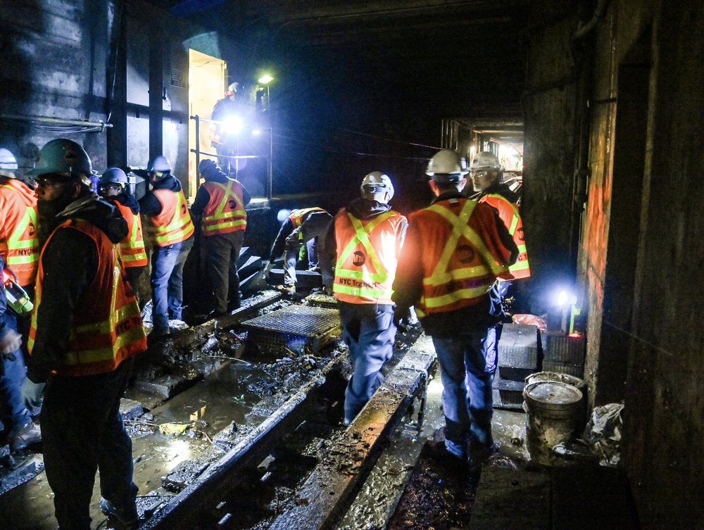 Workers in orange vests on flooded subway tracks.