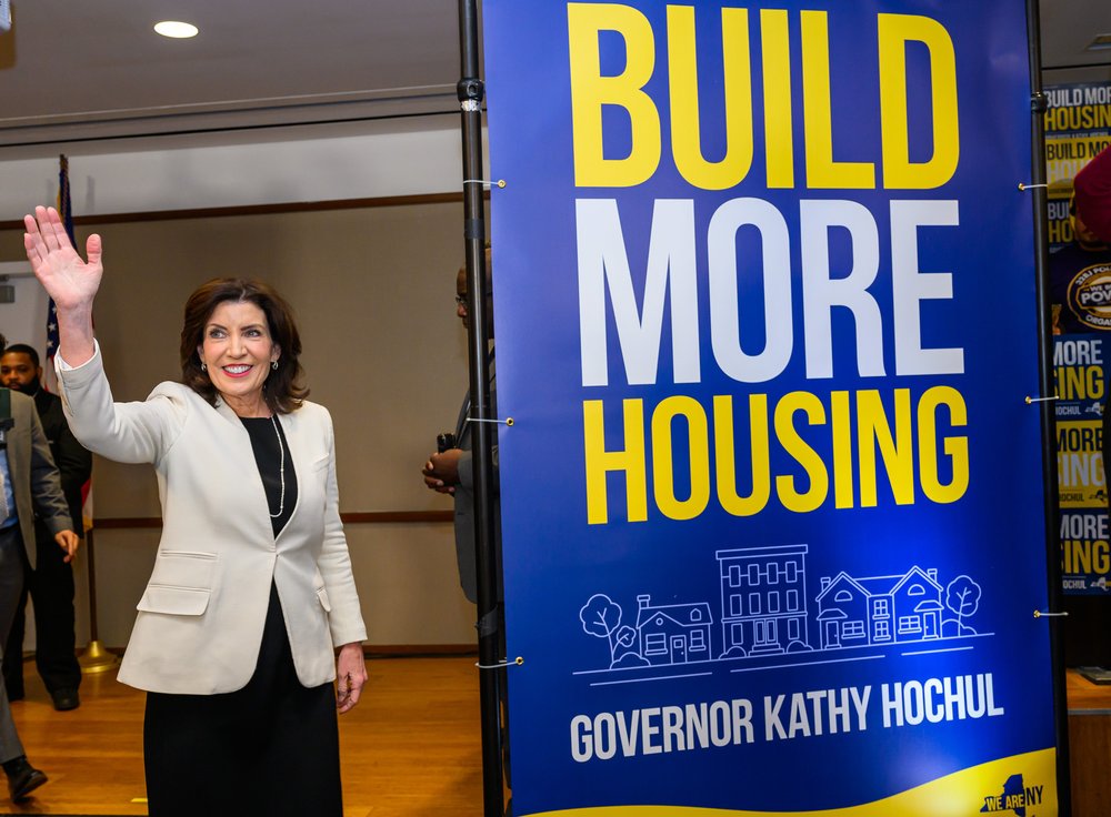Gov. Kathy Hochul stands in front of a sign that says "build more housing."