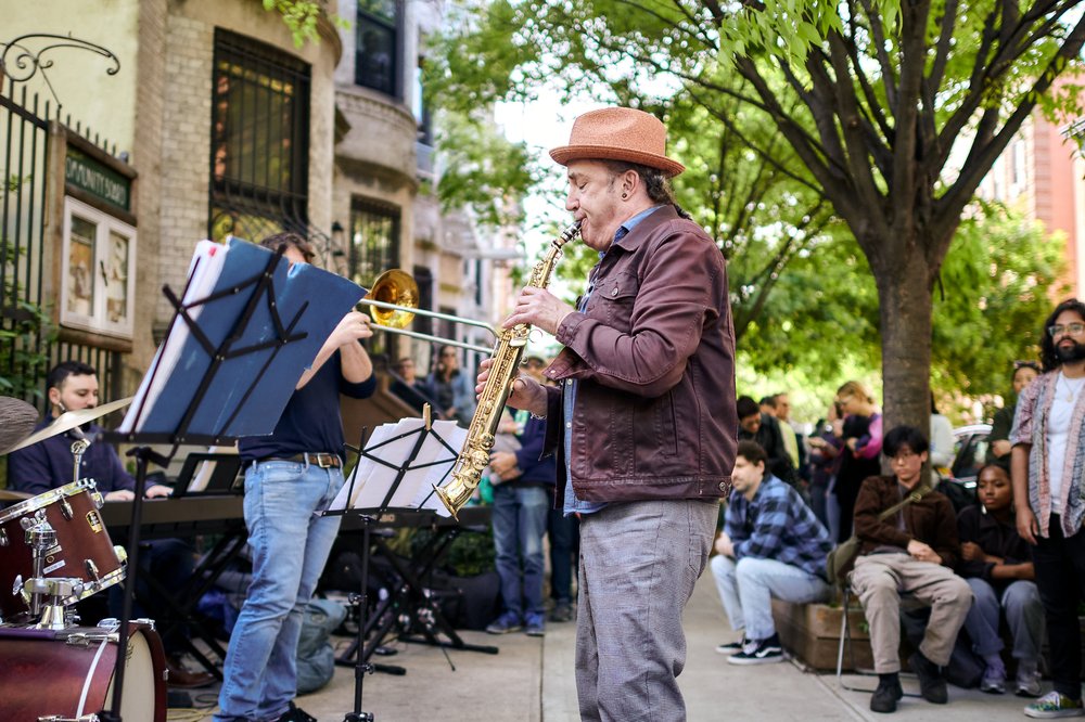A person stands in the street playing a brass instrument.